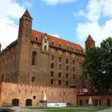 Gotycki zamek, duma kociewie miasta, z czerwonej cegły, z wieżami i czerwonym dachem, pod błękitnym niebem.