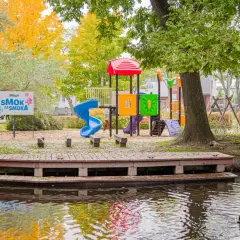 Kolorowy plac zabaw i pomost nad wodą w Rumi. Jesienne liście i tablica "SMOK ZA SMOKA" zapraszają do zabawy.