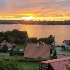 Zachód słońca nad jeziorem, domki letniskowe i zieleń. Tamowa Chmielno w złotej poświacie.