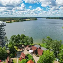 Wieża widokowa w **Kaszubskim Parku Narodowym** nad jeziorem, z żaglówką na wodzie i lasami w tle.