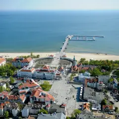Widok na Sopot, część Trójmiasta. Widoczny deptak, plaża, molo i budynki z czerwonymi dachami.