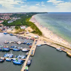 Port rybacki Władysławowo tętni życiem. Wiele łodzi cumuje, a plaża pełna jest wypoczywających.