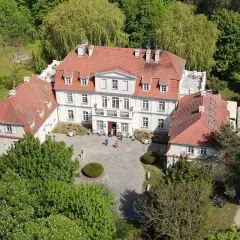 Piękny pałac Godętowo otoczony zielenią. Kilka osób spaceruje po dziedzińcu.