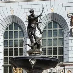 Fontanna Neptuna w Gdańsku, z bogatą rzeźbą boga mórz na tle zabytkowej kamienicy.