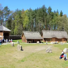 Osada sławutowo: drewniane chaty kryte strzechą, drewniana wieża, ludzie zwiedzają.