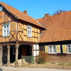 Stary dom podcieniowy z cegły i drewna, z charakterystycznymi drewnianymi słupami podtrzymującymi górną kondygnację.