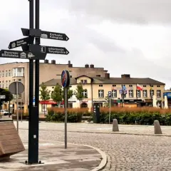 Kartuzy rynek z drogowskazami do kolegiaty, muzeum, dworca i informacji turystycznej. Na pierwszym planie przewrócony kosz.