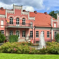 Pałac Przebendowskich w Wejherowie, różowy, z fontanną i kwitnącymi krzewami róż.
