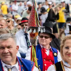 Stare i nowe brusy na festynie. Ludzie w tradycyjnych strojach, wśród nich mężczyzna z kolorową laską.