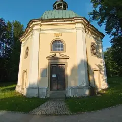 Ośmiokątna kaplica św. Jerzego z zieloną kopułą, otoczona drzewami i zieloną trawą.