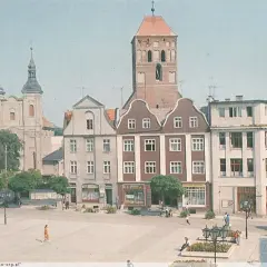 Chojnice rynek z kościołem i kamienicami. Ludzie spacerują po placu, tworząc tętniące życiem tło dla zabytkowej architektury.