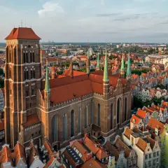 Majestatyczny kościół Mariacki w Gdańsku góruje nad miastem, otoczony kamienicami o czerwonych dachach.