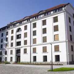 Nowoczesny, biały spichlerz w Słupsku z charakterystycznymi oknami z drewnianymi żaluzjami.