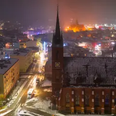 Nocna panorama Kościerzyny zimową porą. Widać ośnieżony kościół, oświetloną ulicę i kolorowe budynki. To piękne kościerzyna atrakcje.