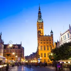Wieczorny widok na Długi Targ, gdzie góruje ratusz Głównego Miasta w Gdańsku. Tętniące życiem kawiarnie i spacerujący ludzie.