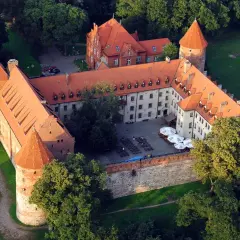 Zamek w Bytowie otoczony zielenią, z czerwonymi dachami i dziedzińcem.