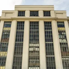 Fasada budynku z cegły i jasnego tynku, z rzędami dużych, prostokątnych okien. To przykład charakterystycznego modernizmu w Gdyni.