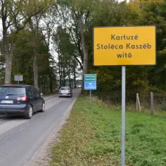 Żółty znak informuje: Kartuzë, Stolëca Kaszëb witô. Droga prowadzi do stolicy Kaszub.