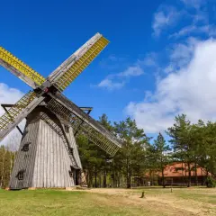 Drewniany wiatrak na Kaszubach, z żółtymi skrzydłami, stoi na tle błękitnego nieba z chmurami.