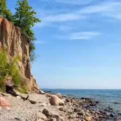 Klif Orłowski z zielenią na szczycie i kamienistą plażą u podnóża. Błękitne niebo i spokojne morze.