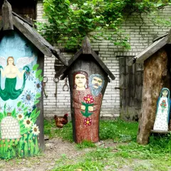 Trzy ozdobne ule, jeden z syreną, drugi z parą ludzi, trzeci z figurką Matki Boskiej. W tle kura i zielona roślinność. Brusy jaglie.
