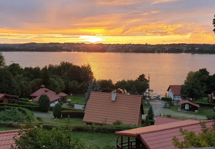 Zachód słońca nad jeziorem, domki letniskowe i zieleń. Tamowa Chmielno w złotej poświacie.