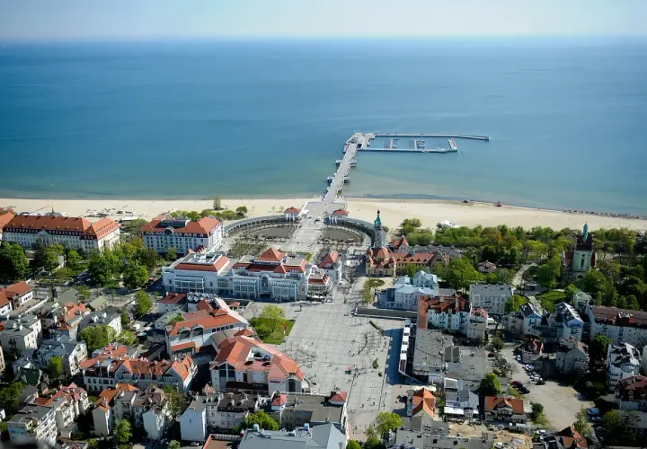 Widok na Sopot, część Trójmiasta. Widoczny deptak, plaża, molo i budynki z czerwonymi dachami.