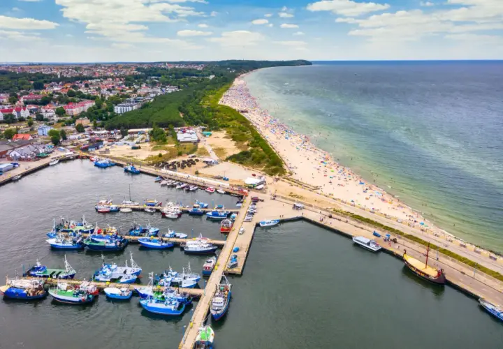 Port rybacki Władysławowo tętni życiem. Wiele łodzi cumuje, a plaża pełna jest wypoczywających.