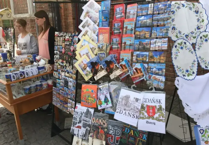 Stoisko z pamiątkami na gdansk market: pocztówki, magnesy i kubki z widokami miasta.