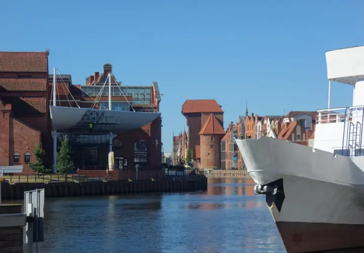 Widok na Motławę w Gdańsku. Na pierwszym planie biały dziób statku, w tle zabytkowe kamienice i Żuraw. Gdańsk starówka zachwyca.