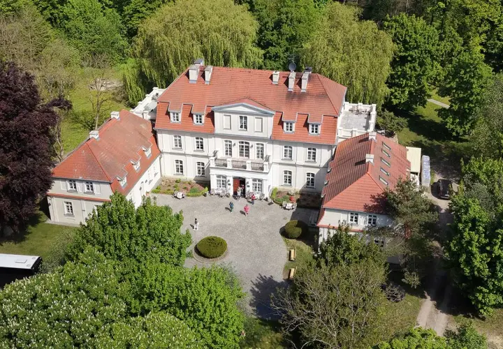 Piękny pałac Godętowo otoczony zielenią. Kilka osób spaceruje po dziedzińcu.