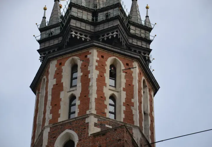 Wieża Kościoła Mariackiego w Krakowie, z cegły i kamienia, z charakterystycznymi oknami i zdobieniami.
