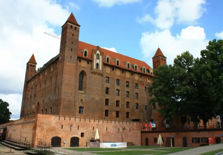 Gotycki zamek, duma kociewie miasta, z czerwonej cegły, z wieżami i czerwonym dachem, pod błękitnym niebem.