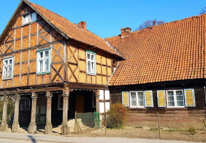 Stary dom podcieniowy z cegły i drewna, z charakterystycznymi drewnianymi słupami podtrzymującymi górną kondygnację.