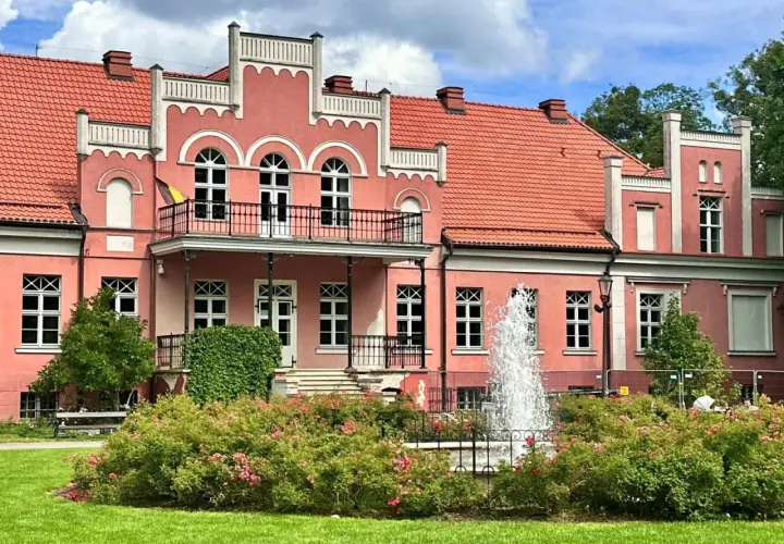 Pałac Przebendowskich w Wejherowie, różowy, z fontanną i kwitnącymi krzewami róż.