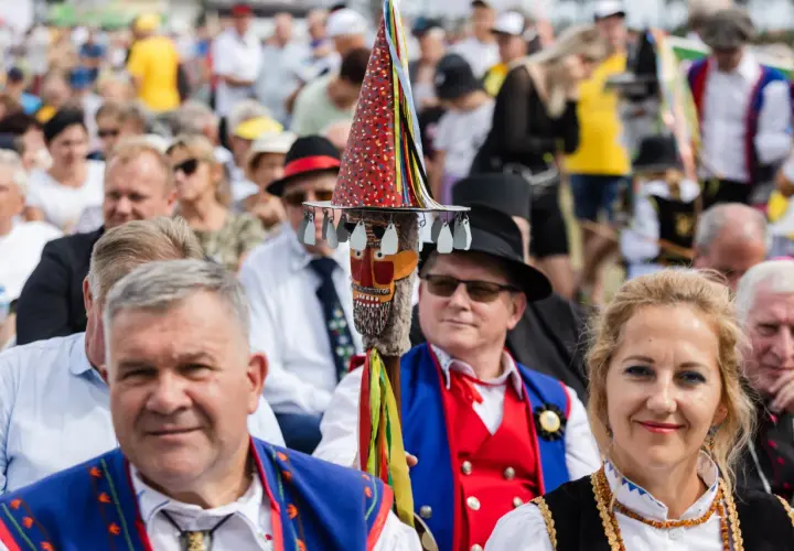 Stare i nowe brusy na festynie. Ludzie w tradycyjnych strojach, wśród nich mężczyzna z kolorową laską.