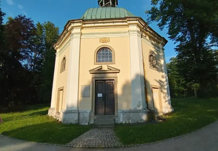 Ośmiokątna kaplica św. Jerzego z zieloną kopułą, otoczona drzewami i zieloną trawą.