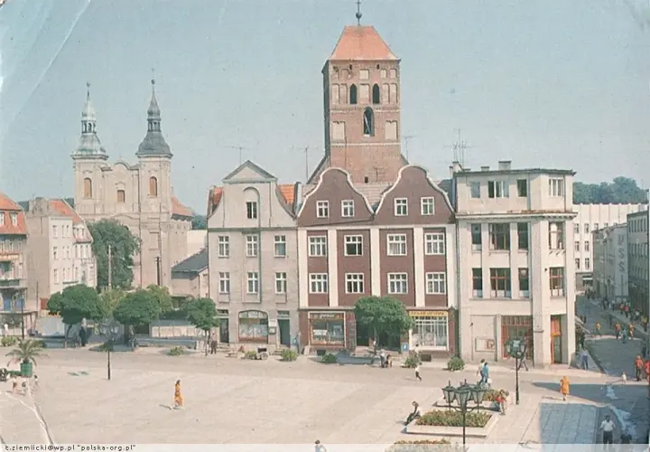 Chojnice rynek z kościołem i kamienicami. Ludzie spacerują po placu, tworząc tętniące życiem tło dla zabytkowej architektury.