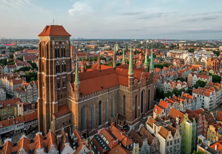 Majestatyczny kościół Mariacki w Gdańsku góruje nad miastem, otoczony kamienicami o czerwonych dachach.
