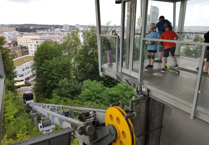 Dzieci na hulajnogach czekają na wjazd kolejką na kamienną górę w Gdyni, podziwiając panoramę miasta.