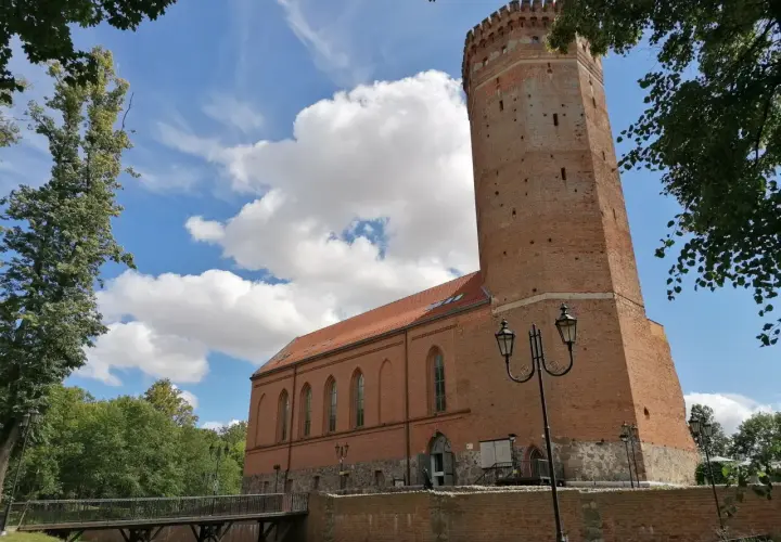 Chojnice zamek krzyżacki, ceglana wieża i budynek muzeum pod błękitnym niebem z chmurami.