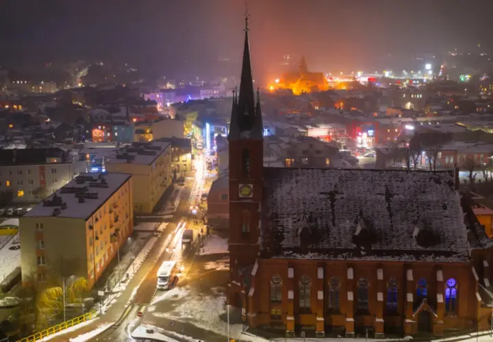 Nocna panorama Kościerzyny zimową porą. Widać ośnieżony kościół, oświetloną ulicę i kolorowe budynki. To piękne kościerzyna atrakcje.