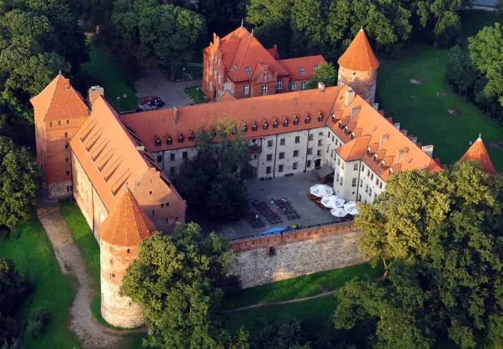 Zamek w Bytowie otoczony zielenią, z czerwonymi dachami i dziedzińcem.