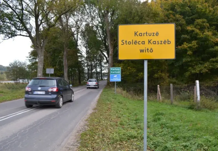 Żółty znak informuje: Kartuzë, Stolëca Kaszëb witô. Droga prowadzi do stolicy Kaszub.
