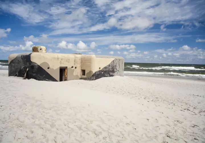 Betonowy bunkier z kamuflażem na piaszczystej plaży w Jastarni. Morze i niebo z chmurami w tle.
