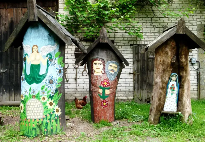 Trzy ozdobne ule, jeden z syreną, drugi z parą ludzi, trzeci z figurką Matki Boskiej. W tle kura i zielona roślinność. Brusy jaglie.