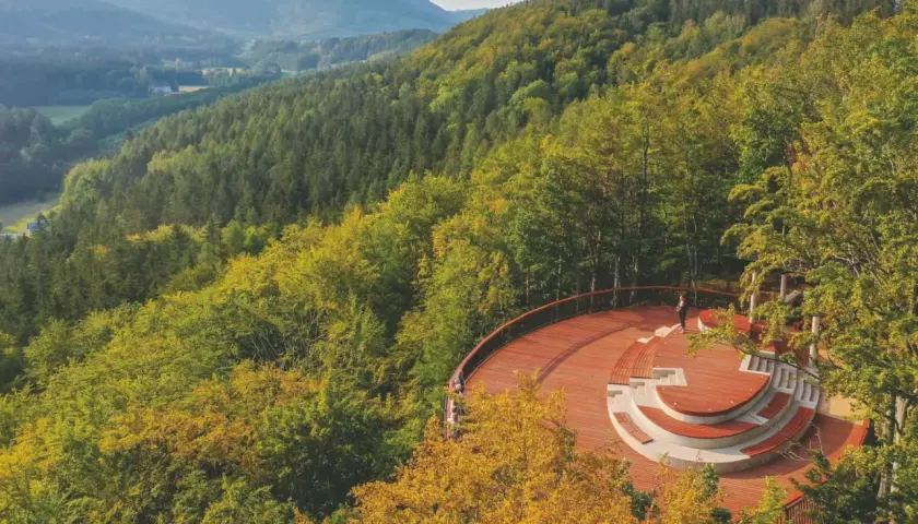 Drewniane wierze widokowe z amfiteatrem otoczone jesiennym lasem. W oddali góry i dolina.