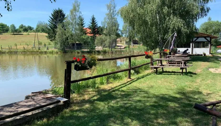 Urokliwe miejsce nad potokiem grzędy. Drewniane ławki i stoły zapraszają do odpoczynku, a kwitnące kwiaty dodają kolorytu.