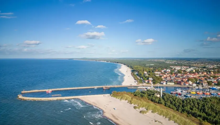 Malownicza plaża w Ustce z widokiem na port, morze i miasto. Słoneczny dzień zachęca do wypoczynku.