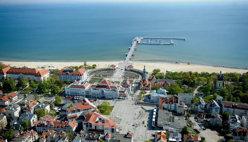 Widok na Sopot, część Trójmiasta. Widoczny deptak, plaża, molo i budynki z czerwonymi dachami.